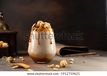 Sweet Milkshake with caramel syrup,cream liqueur,caramel popcorn and chocolate powder on brown background with vintage,manual coffee grinder. Royalty-Free Stock Photo #1912759621