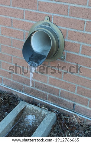 Stream of water is frozen as it falls from a drainpipe