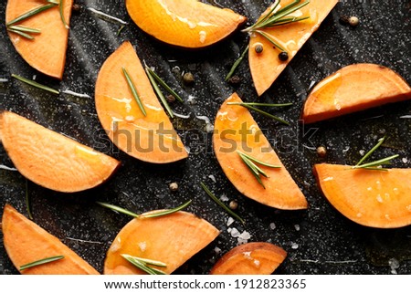 Composition of sliced sweet potatoes in a grill pan, rosemary spice, knife, salt, vegetable oil, kitchen board, top view. Space for text.