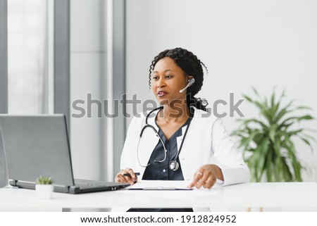 medicine, online service and healthcare concept - happy smiling african american female doctor or nurse with headset and laptop having conference or video call at hospital Royalty-Free Stock Photo #1912824952