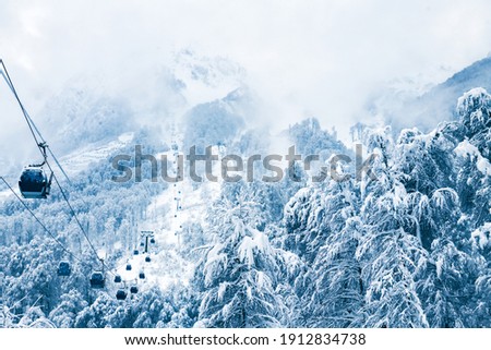 Gondola lift in ski resort in winter mountains during snowfall. Rosa Khutor, Sochi, Russia. Beautiful snow-covered forest, winter landscape Royalty-Free Stock Photo #1912834738