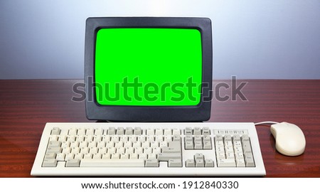 An old retro CRT monitor with a green screen for adding video and images with a 1990 keyboard sits on a brown vintage table. Old retro computer.