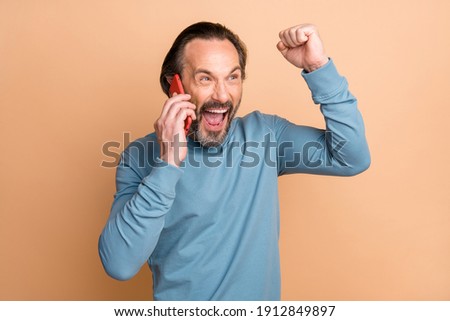 Photo portrait of happy man talking on cellphone laughing loudly crazy gesturing won lottery isolated on pastel beige color background