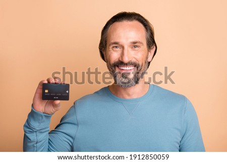 Photo portrait of middle-aged man showing credit debit card smiling isolated on pastel beige color background