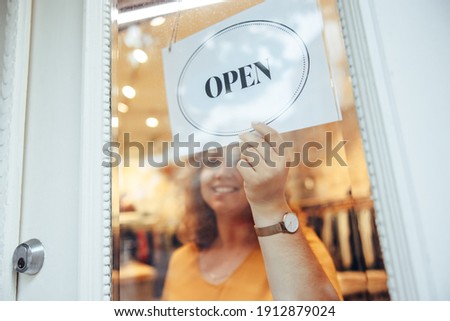 Business owner holding and turning sign to open on storefront door. Woman hanging Open sign on her store door.
