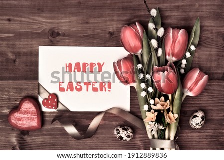 Card with text Overhead view, flat lay. Arrangement of Easter, springtime decorations. Wrapped gifts, red tulips, pussy willow, lily of valley flowers. Easter eggs, hearts, ribbons on brown wood.
