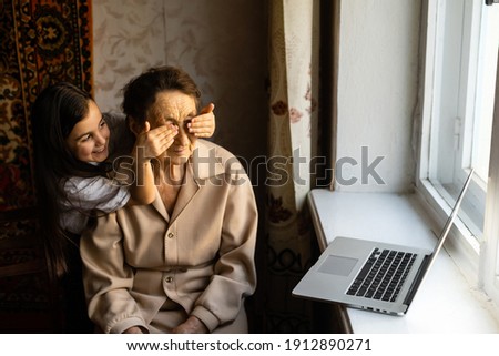 Happy senior woman sitting with her granddaughter looking at laptop making video call. Mature lady talking to webcam, doing online chat at home during self isolation. Family time during Corona