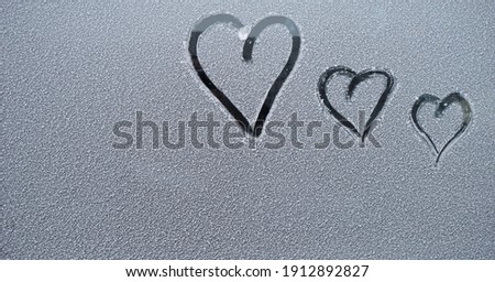   three finger-drawn hearts on snow-covered glass                              Royalty-Free Stock Photo #1912892827