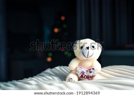 Close-up of child stuffed toy on white silk material. Photoshoot of Teddy bear with heart. Valentines day or christmas and gifts concept. Copy space in left side. Lights on dark background