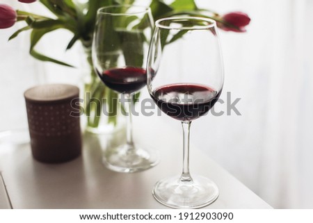 Two glasses of red wine, a bouquet of tulips on a white table, romantic atmosphere  
