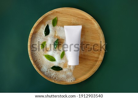 Top view mockup facial skincare white tube product bottle with blank label and soap bubbles with fresh green leaves on top Tidewater Green solid color plain isolated background Royalty-Free Stock Photo #1912903540
