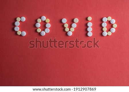 Flat lay of medicine pills shape as word covid 19 with syringe and pills on red background