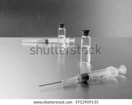 Syringes and ampoules on a polished metal background. Coronavirus vaccination and immunization concept. Selective focus. Black and white monochrome image. Copy space.