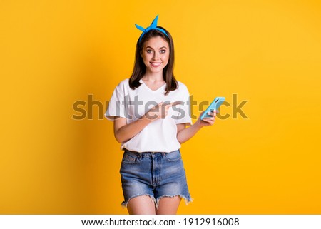 Photo portrait of girl pointing with finger at smartphone smiling recommending isolated on vibrant yellow color background