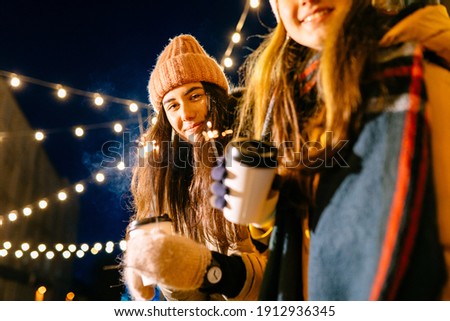 Amazing women friends in gray coat and pink hat walking down the street with sparkler. Adorable females students in winter outfit spending time outdoor and looking at Bengal light with smile. Royalty-Free Stock Photo #1912936345