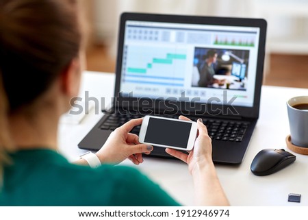 technology, post production and vlog concept - close up of woman with smartphone and laptop computer working at home office