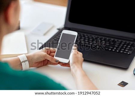 business, technology and people concept - close up of woman with smartphone and laptop computer working at home office