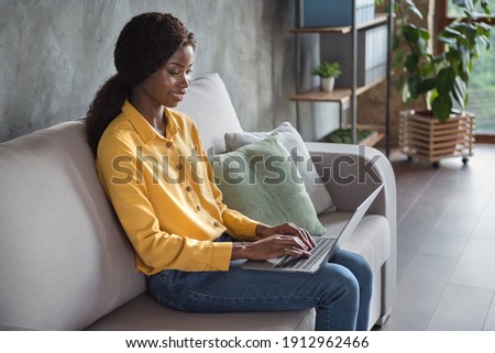 Photo portrait of african american woman sitting on couch working on laptop in modern office indoors
