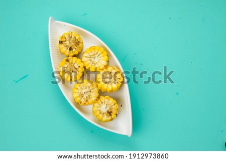 Corn, a snack made using ripe corn and garnished with chilli flakes and honey arranged in a white beautiful tableware  which is placed on a solid ice blue colour , isolated.