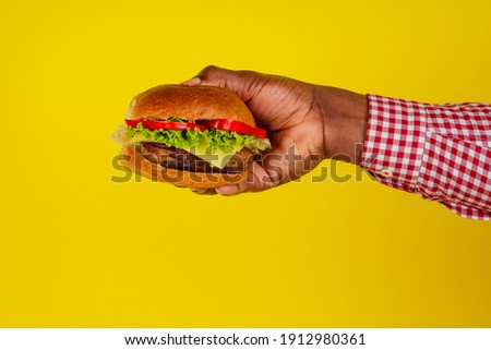 young african american man eating hamburger isolated on yellow background hands close up