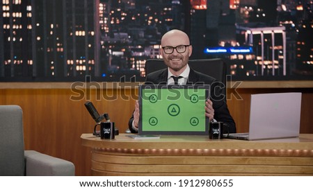 Late-night talk show host showing a green board with tracking points to audience in a studio. TV broadcast style show