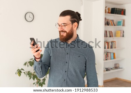Photo of bearded man in casual using smartphone in office.