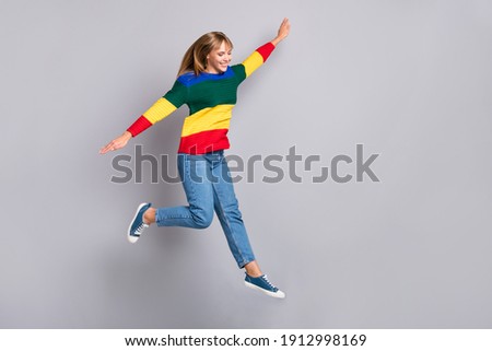 Full length body size photo of funny playful girl jumping high plane wings colorful sweater isolated on pastel grey color background