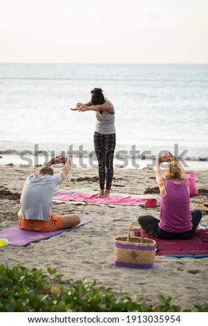 Women doing yoga exercises or supported pigeon pose on an empty beach of the Indian ocean in Mauritius