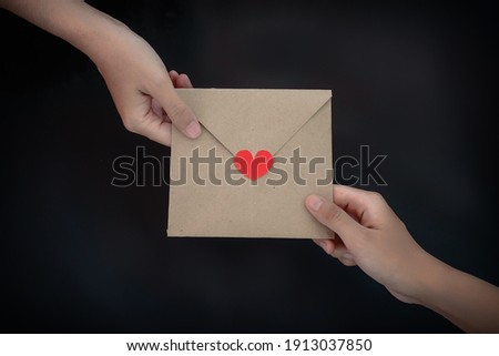 Close-up of Women giving card letter with red heart on the table, black background. Concept of creating handmade gifts for Valentine's Day or other days holiday
