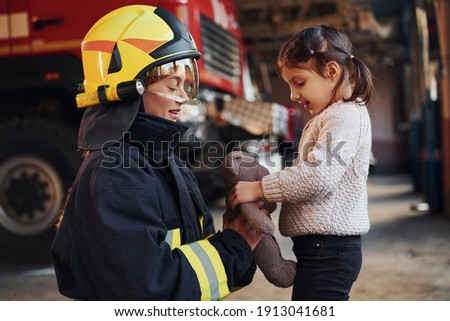 Happy little girl is with female firefighter in protective uniform.