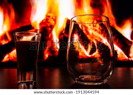A beautiful glass with a drink near the fireplace. Firewood and fire. Glass and liquid.