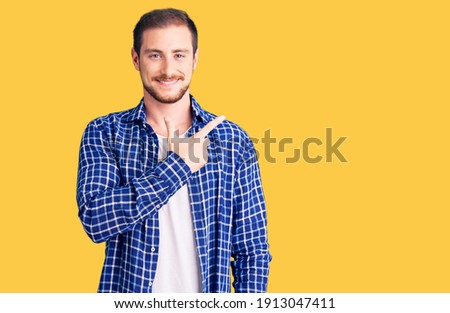 Young handsome caucasian man wearing casual clothes cheerful with a smile of face pointing with hand and finger up to the side with happy and natural expression on face 