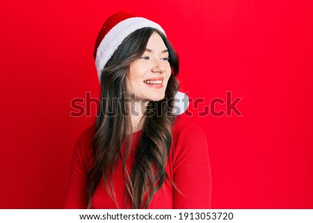 Young beautiful caucasian girl wearing christmas hat looking away to side with smile on face, natural expression. laughing confident. 