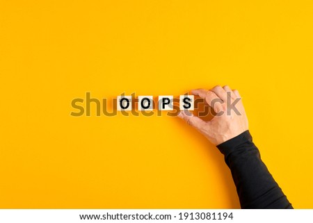 Male hand placing the wooden cubes with the word oops on yellow background. Apologies for a a mistake or error. Royalty-Free Stock Photo #1913081194