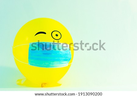 Yellow inflatable ball with a medical mask on a white background with the image of cheerful gestures. The concept of a positive mood during a pandemic