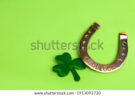 Golden horseshoe and decorative clover leaf on light green background, space for text. Saint Patrick's Day celebration