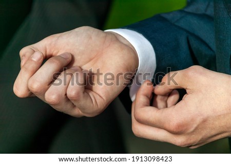 Adult male in a formal wear fashion suit adjusting and fastening his shirt sleeve button at a wedding, stock photo image
