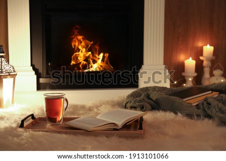 Cup of tea and book on fuzzy rug near fireplace at home. Cozy atmosphere