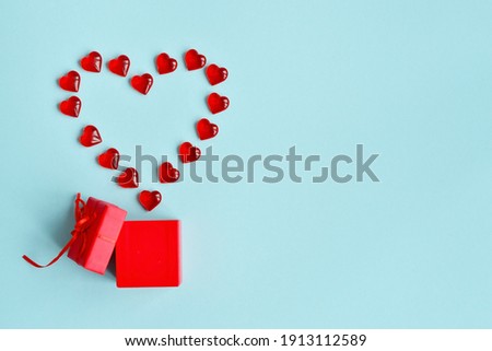 Valentine's Day background. Red gift box and red hearts in pastel blue tones. The concept of Valentine's Day. Flat sunbed, top view, copy space