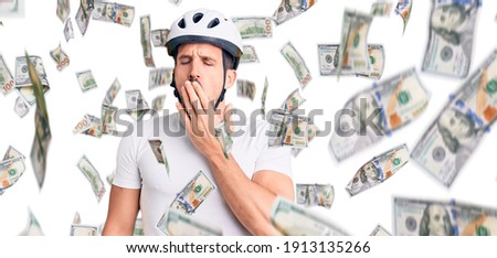 Young handsome man wearing bike helmet bored yawning tired covering mouth with hand. restless and sleepiness.