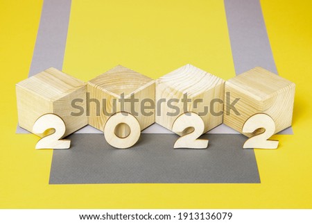 Wooden cubes and numbers 2022 on a yellow and gray paper background. Trendy new year template for design