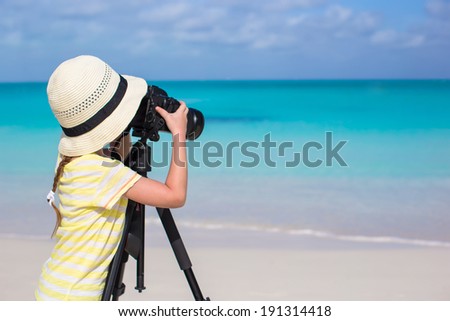 Portrait of a little girl with a camera on a tripod on the white sandy beach