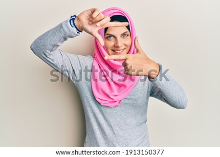 Young caucasian woman wearing traditional islamic hijab scarf smiling making frame with hands and fingers with happy face. creativity and photography concept. 