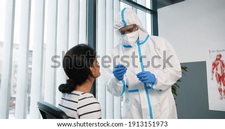Portrait of healthcare worker in protective suit and gloves taking from female young patient sample for analysis and coronavirus test working in hospital laboratory, covid pandemic concept Royalty-Free Stock Photo #1913151973