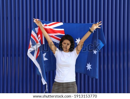 pretty lady is holding Australia flag in her hands and raising to the end of the arm at the back on blue background.
