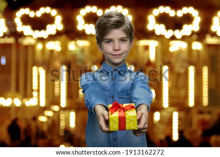 Cute little boy is giving you a present. Glowing city lights on the background.