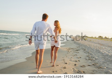 Young beautiful couple walks along the seashore at sunset. Honeymoon. Romantic trip. Royalty-Free Stock Photo #1913168284