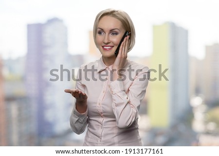 Successful blonde woman is talking on the phone. American businesswoman is making a deal. Blurred high-rise building on the background.