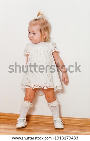Cute half-old blonde girl in a white dress and full-length golf cart poses
