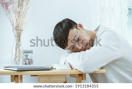 Asian handsome man wearing eyeglasses, getting tired from his overload work and taking a nap on table at home. Lifestyle and New Normal Concept.